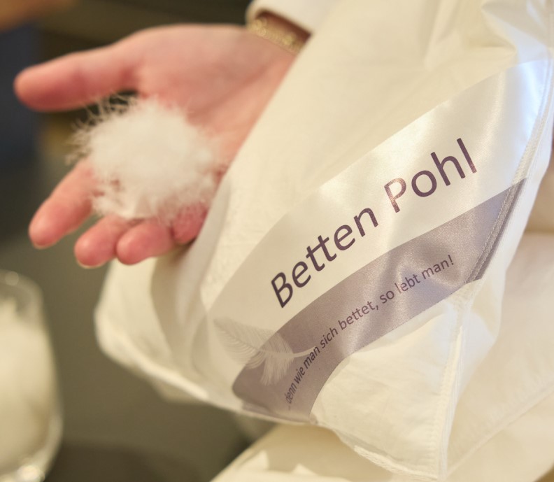 Hand die neben eine Betten Pohl Decke eine handvoll Daunen hält